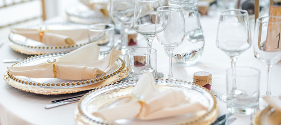 A set weddign table full of glassware, silverware, linens and plates