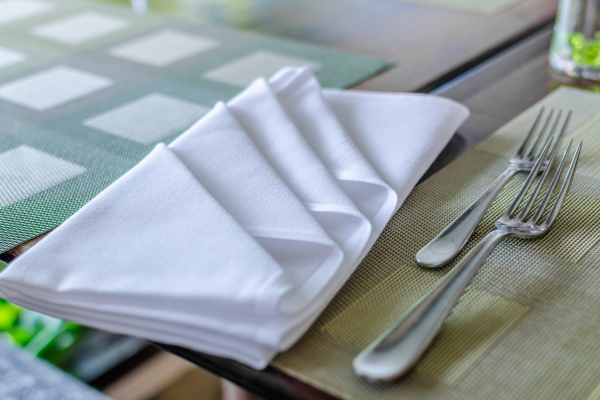 A folded white napkin set on a table next to a fork